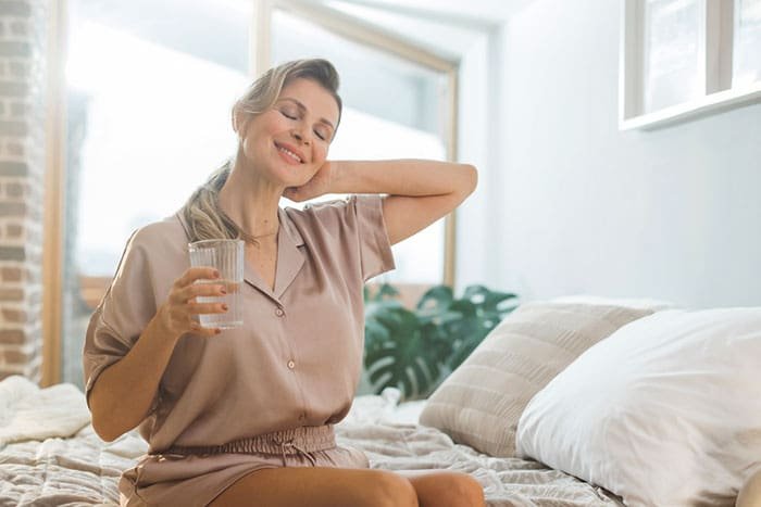 a female on her bed holding a half glass of water in her night suit
