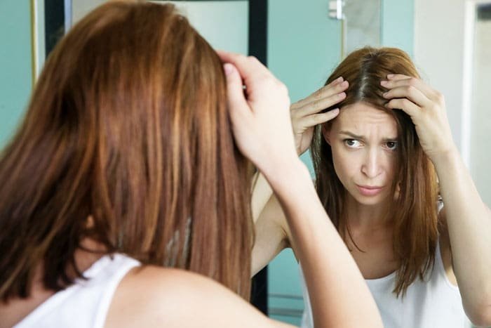 a female looks worried after checking her hair in mirror