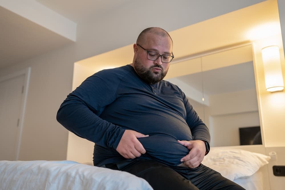 Fat man suffering with obesity sitting on his bed
